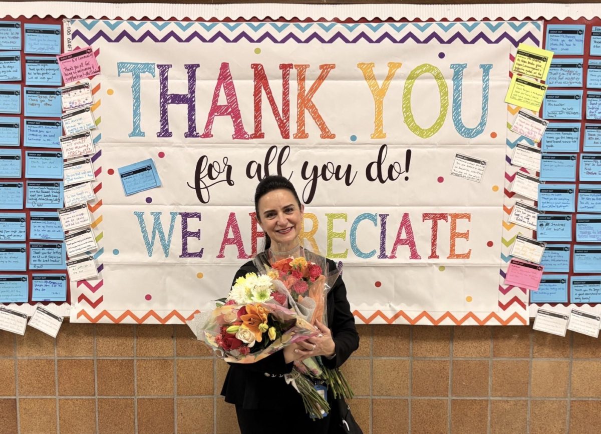 Ms. Mazziotti with flowers in front of a thank you bulletin board.